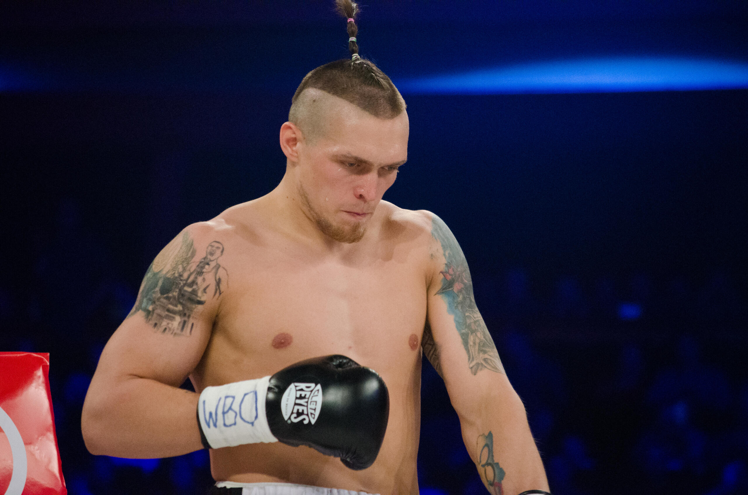 Un boxeador sin camiseta, con un caracter&iacute;stico peinado mohicano y tatuajes en los brazos, que lleva guantes de boxeo negros de la marca Cleto Reyes con las siglas &laquo;WBO&raquo; escritas en ellos.